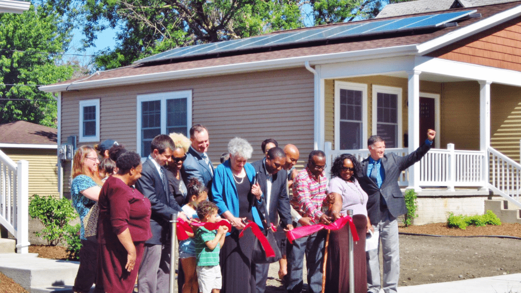 People cutting a ribbon in front of a house with solar panels